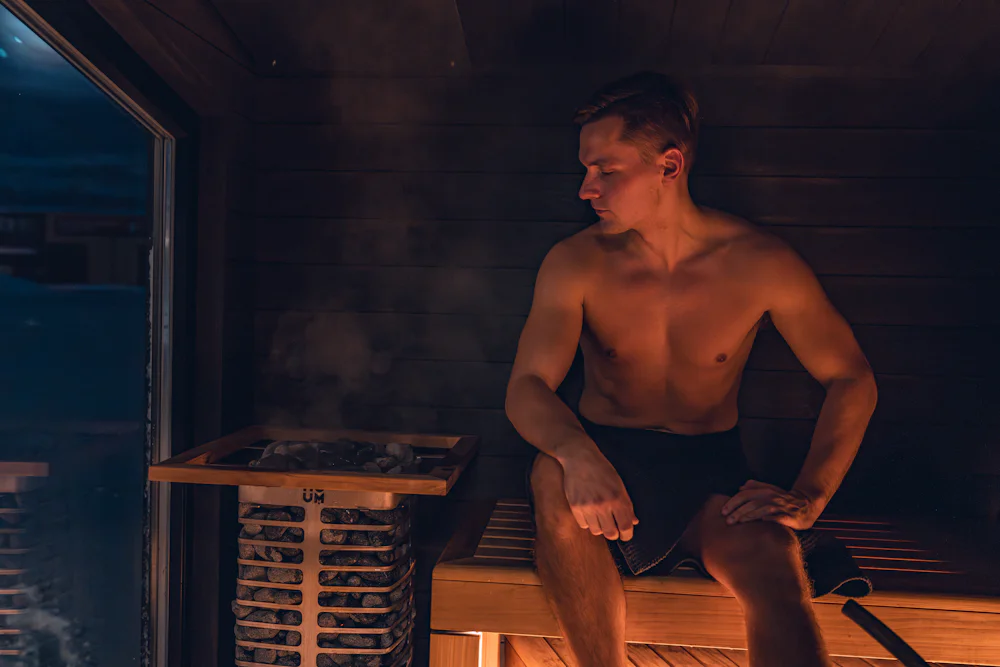 A man sitting on a bench in a dim, warm sauna