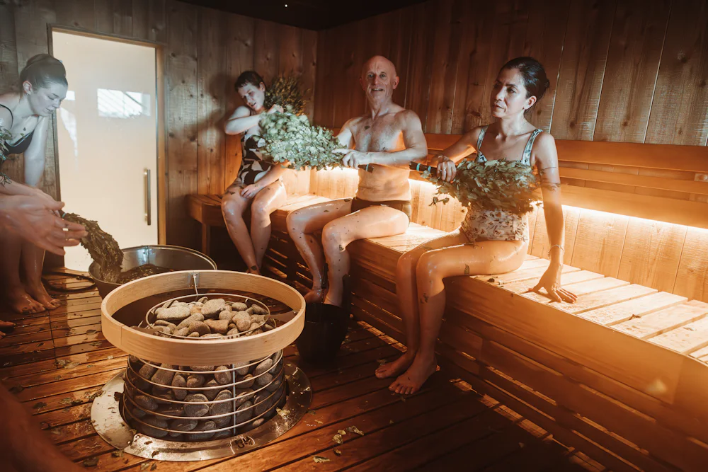 A group of people in a sauna, some holding leafy birch whisks