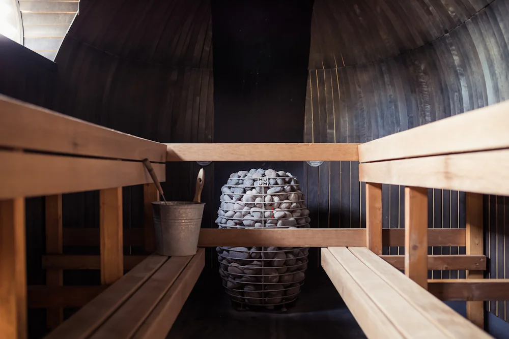 The inside of a barrel sauna with slatted benches and a stove behind a guard