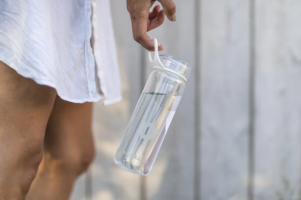 A person holding a water bottle beside a sauna